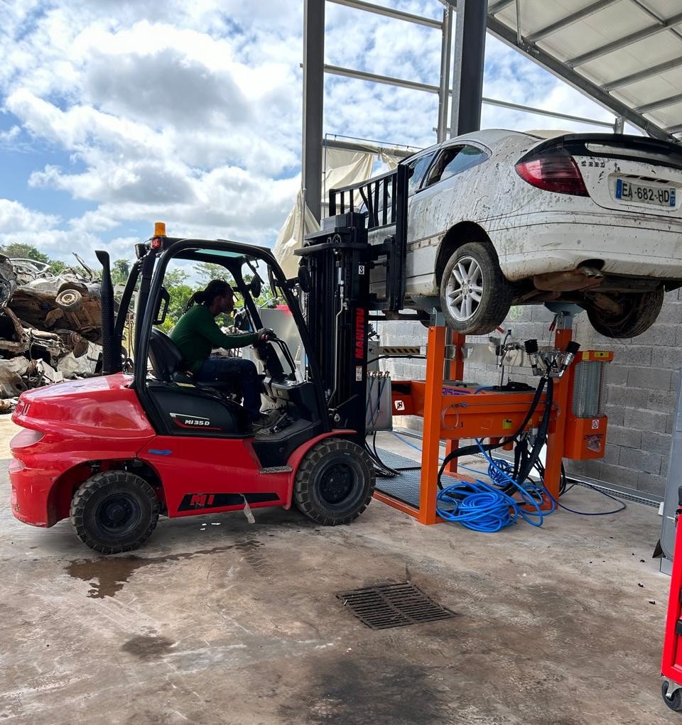 Chariot élévateur soulevant une voiture dans un garage.